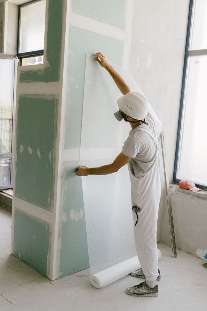 Mastering the First Impression: Your intriguing post title goes here Construction worker in hard hat applying wallpaper inside a building under renovation.